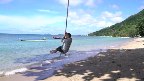 Чоловік гойдається на мотузці на пляжі на березі моря — стокове відео