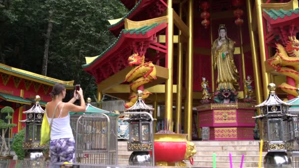 Женщина фотографирует статую божества в буддийском храме — стоковое видео