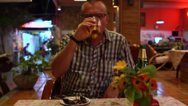 Ein Mann trinkt Bier und isst eine gebratene Heuschrecke in einem thailändischen Restaurant — Stockvideo