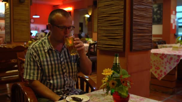 Ein Mann trinkt Bier und isst eine gebratene Kakerlake in einem thailändischen Restaurant — Stockvideo