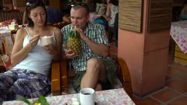 Un uomo e una donna sono seduti in un ristorante a mangiare gelato e bere succo d'ananas — Video Stock