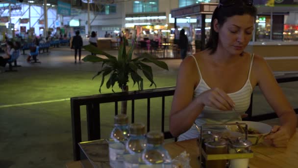 Une femme est assise dans un café de la gare et ajoute de l'assaisonnement à Pad Thai — Video