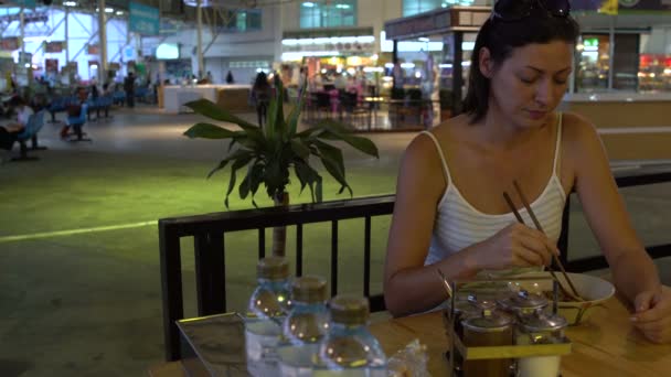 Una mujer en la cafetería de la estación comiendo palos Pad Thai — Vídeo de stock