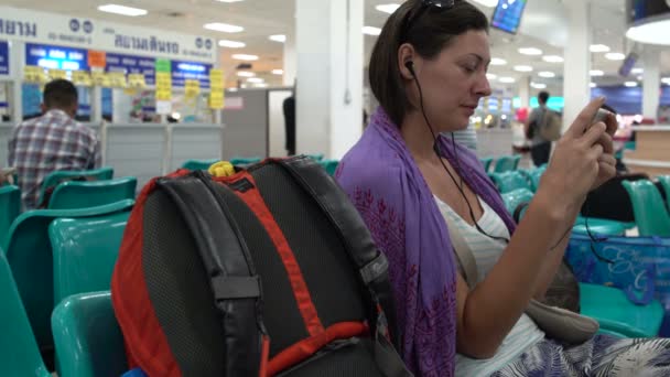 Uma mulher senta-se em uma sala de espera com um Smartphone — Vídeo de Stock