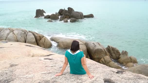 Kvinnan som sitter på stenarna på stranden — Stockvideo