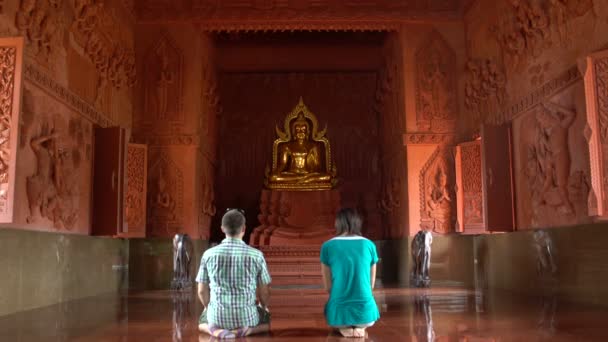 En kvinna och en man be medan knästående framför en buddhastaty i ett buddhistiskt tempel — Stockvideo