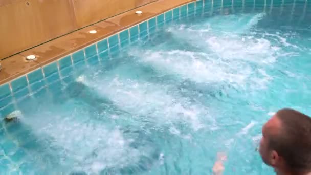 Mann schwimmt zum Whirlpool und sitzt darin — Stockvideo