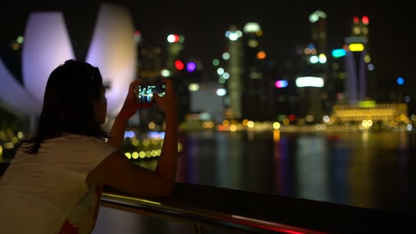 Una mujer está tomando fotos de una ciudad nocturna en un teléfono inteligente — Vídeos de Stock