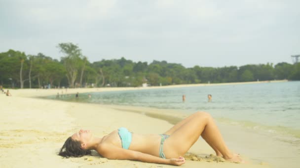 A woman is sunbathing lying on the sand. A man is bracing a woman with water — Stock Video