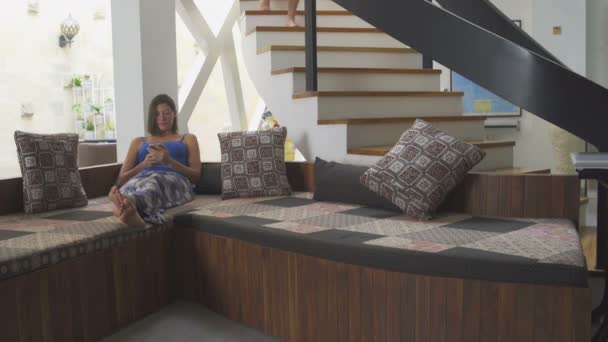 スマート フォンを持つ女性はソファに横たわっています。男が階段を下る — ストック動画
