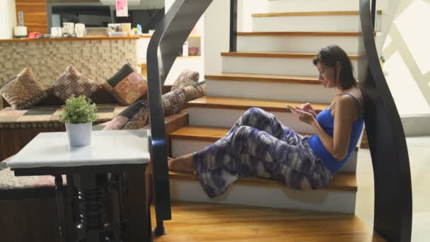 Una ragazza con uno smartphone si siede sulle scale della casa. L'uomo scende le scale. — Video Stock