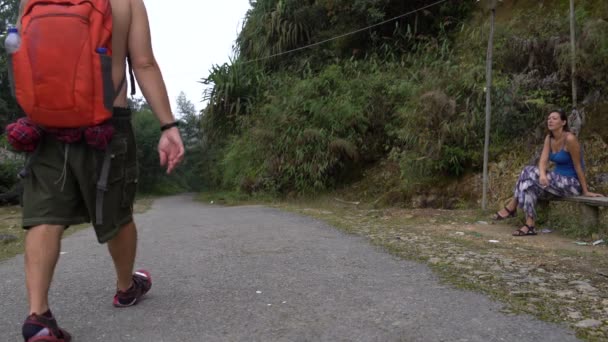 Una mujer fuma sentada en un banco del parque. Un turista con una mochila camina por la carretera — Vídeos de Stock