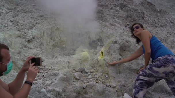 A man is taking pictures of a woman next to a fumarole on a smartphone — Stock Video