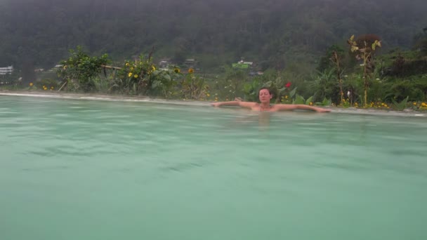 Eine Frau entspannt sich in einer heißen Schwefelwasserstoffquelle am Fuße eines Vulkans — Stockvideo