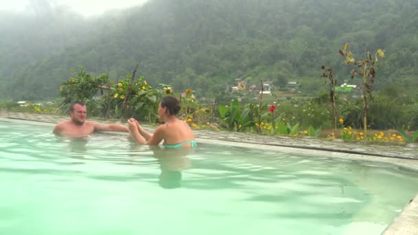 Una mujer está haciendo un masaje de pies de hombre en una piscina con agua caliente de sulfuro de hidrógeno — Vídeos de Stock