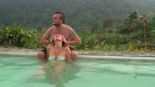 Жінка сидить у гарячому джерелі з тепловою водою. Чоловік масажує голову жінки . — стокове відео