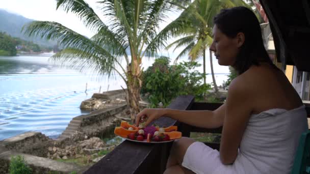 Mujer comiendo fresas sentada en una toalla en el fondo de un lago y montañas — Vídeos de Stock