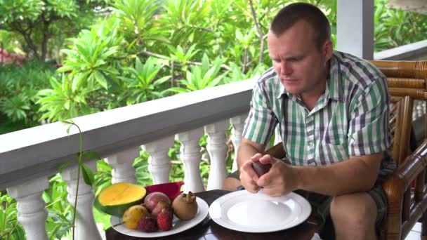 Man sitting on the balcony cleans the Salacca fruit and eats — Stock Video