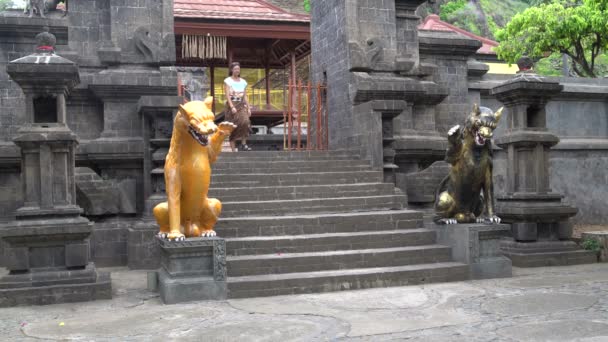 Eine Frau im langen Rock tritt aus einem buddhistischen Tempel hervor und steigt eine Steintreppe mit Statuen hinunter — Stockvideo