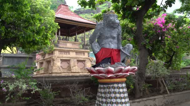 Статуя обезьяны, сидящей на цветке лотоса. В фоновом прыжке обезьяны — стоковое видео
