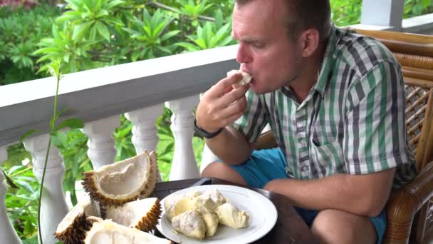 Um homem sentado na varanda comendo durian — Vídeo de Stock