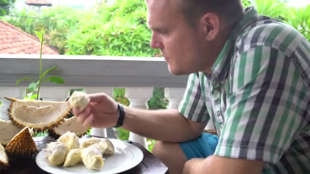 En mand sidder på balkonen ved bordet og spiser durian hænder – Stock-video