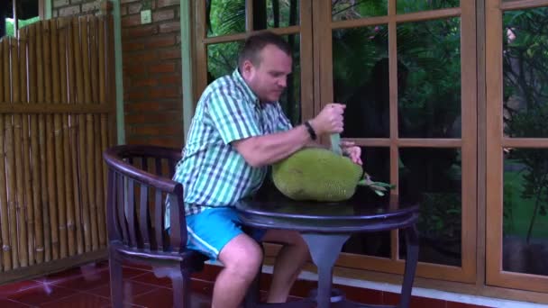 Un hombre sentado en la terraza cortando la jaca con un cuchillo — Vídeo de stock