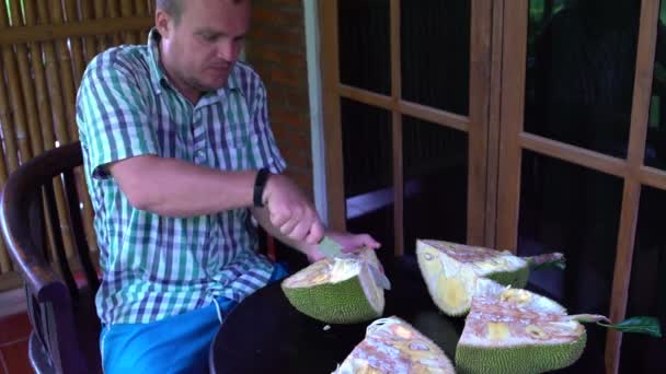 Der Mann, der auf der Terrasse sitzt, reinigt die Jackfrucht — Stockvideo