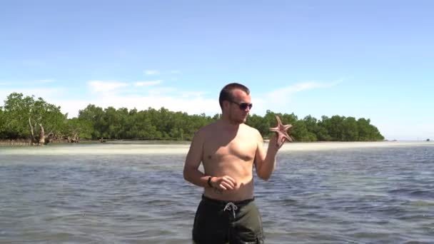 Een man kijken een zeester staande in de zee — Stockvideo