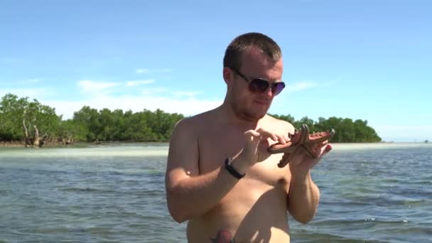 Een man staat op zee en kijkt naar een zeester — Stockvideo