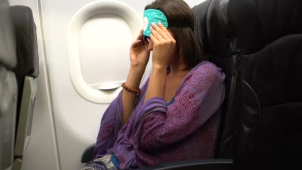 Женщина в самолёте снимает с него маску для сна и открывает иллюминатор — стоковое видео