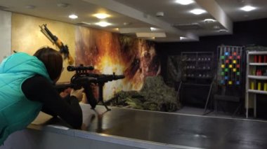 Atış poligonuna. Gözlüklü kadın amaçlayan ve bir Kalaşnikof saldırı tüfeği metal hedeflerini vuruyor.