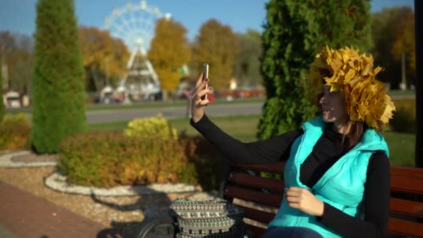 Женщина с кленовым венком на голове делает селфи на смартфоне — стоковое видео