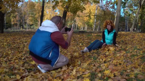 Ein Mann fotografiert, wie eine Frau Laub wegwirft — Stockvideo