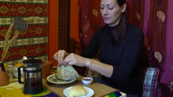 Una donna in un caffè si siede a tavola e mangia una torta immergendola nella salsa. — Video Stock