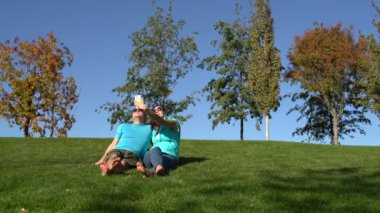 Kadın ve erkek yeşil çimenlerin üzerinde parkta yalınayak oturup bir selfie bir smartphone