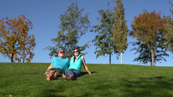 Frau und Mann entspannen sich im Park auf dem grünen Gras sitzend barfuß. ein Mann steht auf und geht — Stockvideo