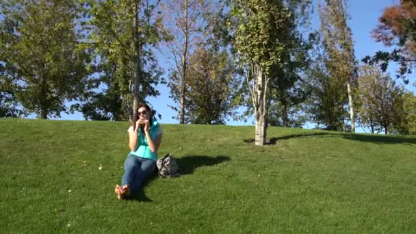 Woman is sitting on the green grass barefoot and eating a pie — Stock Video