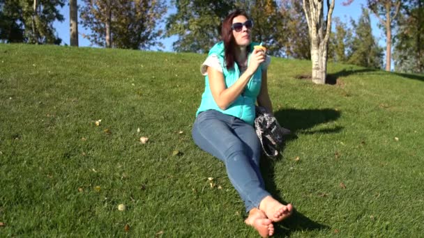 Woman Sits Park Lawn Barefoot Eats Bun — Stock Video