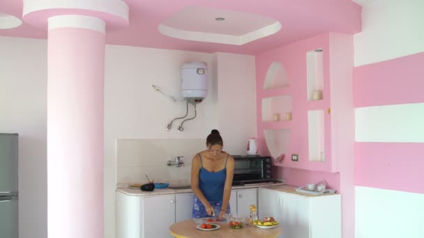 Mujer corta un tomate en una tabla sobre la mesa en la cocina y lo pone en un recipiente para ensaladas — Vídeos de Stock