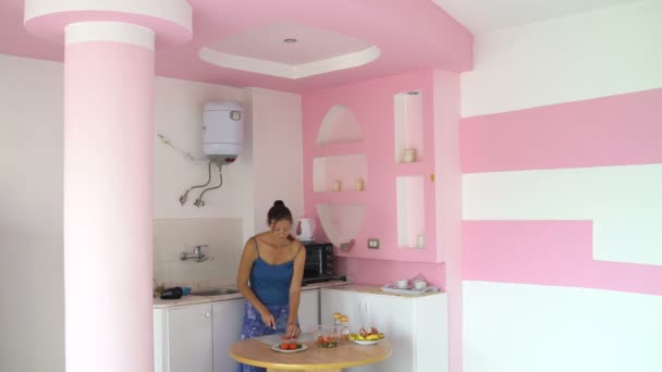 Kadın mutfakta bir masada bir kesme tahtası üzerinde bir domates keser ve bir salata kasesine koyar — Stok video