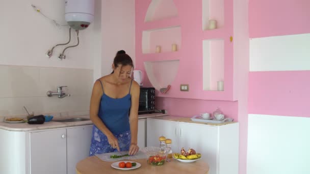 Mujer corta pepino y tomate en una tabla de cortar en una mesa en la cocina — Vídeos de Stock