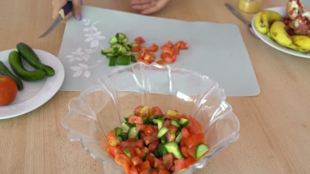Жінка розрізає овочі на обробній дошці на столі на кухні ножем — стокове відео