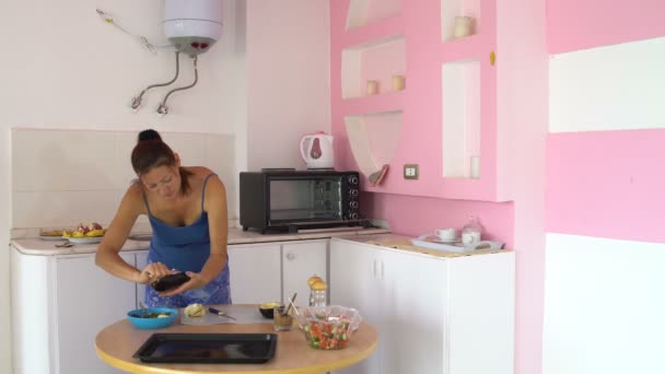 Vrouw in de keuken reinigt aubergine — Stockvideo