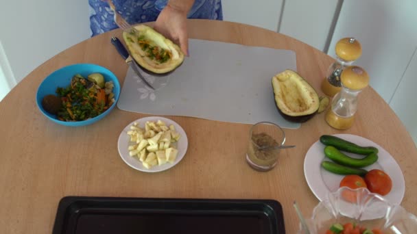 Woman in the kitchen puts vegetables in eggplant — Stock Video