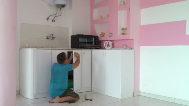Мужчина ремонтирует дверь шкафа на кухне. Женщина приходит, чтобы проверить работу — стоковое видео