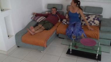 Bir adam kanepede yatıyor ve Tv izliyor. Bir kadın bir dondurma ile geliyor ve ileri oturur