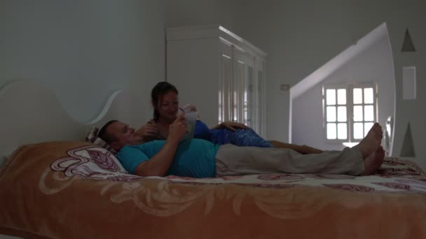 Un uomo e una donna si trovano in camera da letto su un letto e utilizzare il tablet pc. Donna si alza e se ne va — Video Stock