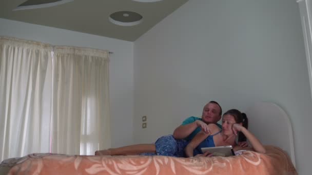 Žena a muž jsou ležet na gauči a použití počítače tablet pc. Muž zvedne a opouští místnost — Stock video