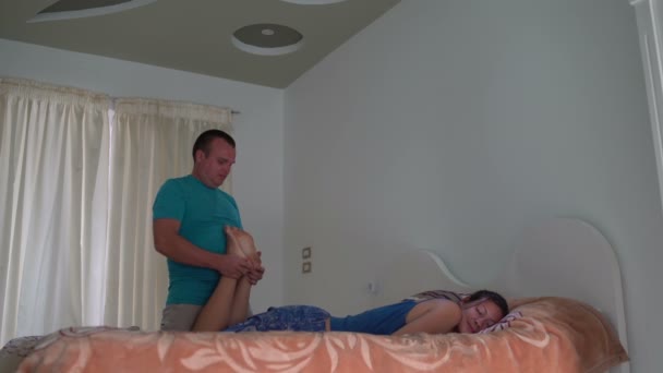 La mujer está acostada en la cama. El hombre hace masaje de pies a la mujer — Vídeo de stock